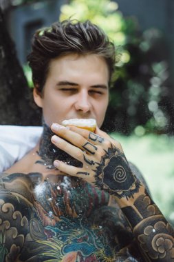 Genç yakışıklı adam açık havada bahçede açık havada yatakta kahvaltı dövme