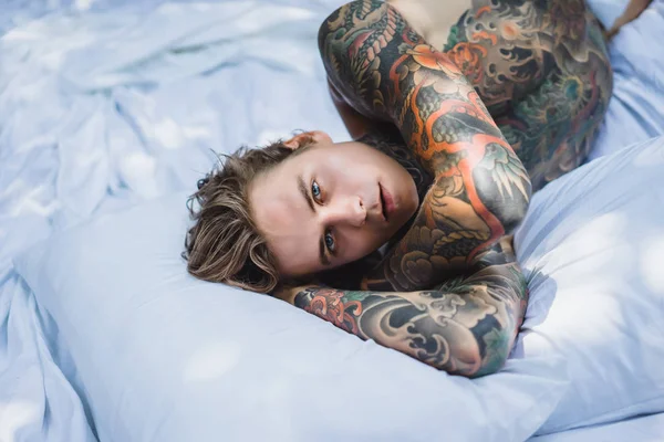 ハンサムな若い入れ墨男の白いベッドでリラックス — ストック写真