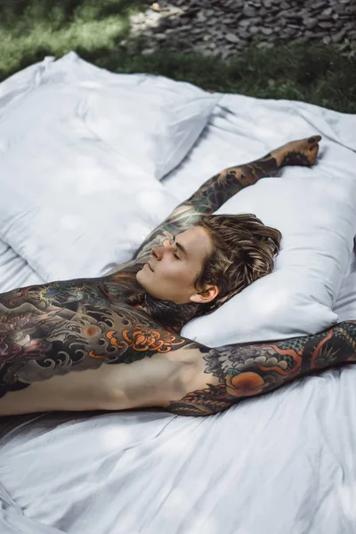 Handsome young tattooed man relaxing on white bed