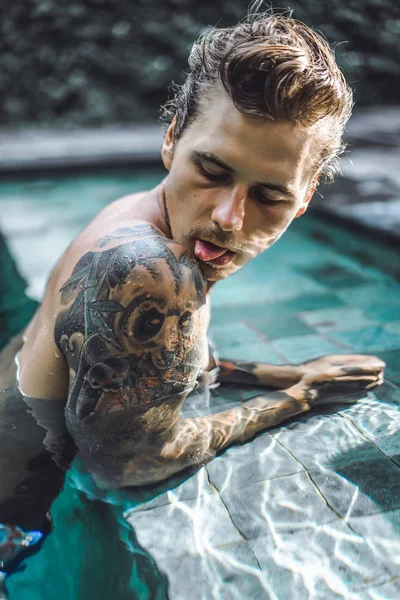年轻英俊的男子在纹身休息在室外游泳池 泳池里有个纹身的男人玩得很开心 在印度尼西亚巴厘岛 — 图库照片