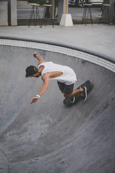 Bir havuzda pateni bir şık genç adam bir skatepark, bir kaykay üzerinde beyaz bir T-shirt ve şapka paten.