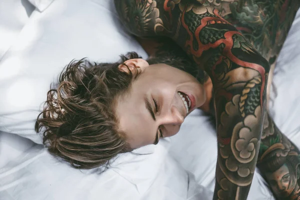 Handsome young tattooed man relaxing on white bed