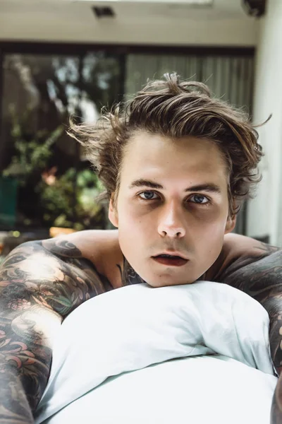 a young handsome tattooed man in the morning in bed tosses up the pillows. bed in the garden