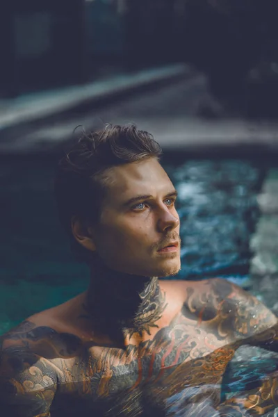 young handsome man in tattoos resting in the outdoor pool. A tattooed man in the pool is having fun. on bali, indonesia