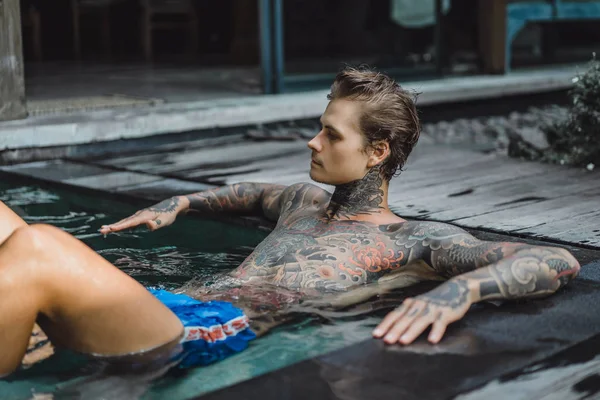 young handsome man in tattoos resting in the outdoor pool. A tattooed man in the pool is having fun. on bali, indonesia