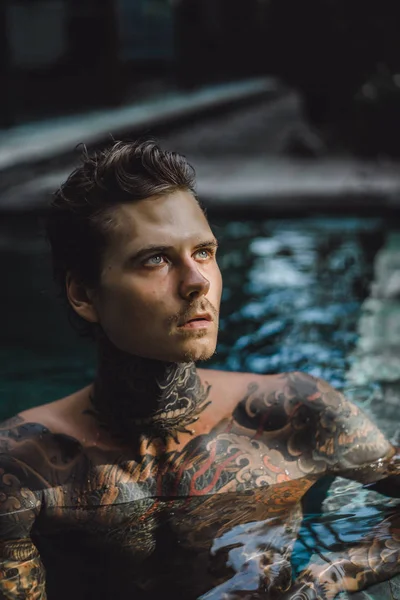 young handsome man in tattoos resting in the outdoor pool. A tattooed man in the pool is having fun. on bali, indonesia