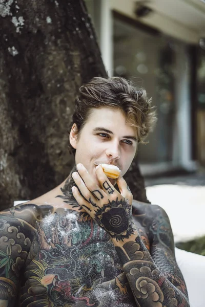 Genç yakışıklı adam açık havada bahçede açık havada yatakta kahvaltı dövme