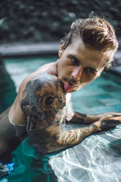 年轻英俊的男子在纹身休息在室外游泳池 泳池里有个纹身的男人玩得很开心 在印度尼西亚巴厘岛 — 图库照片