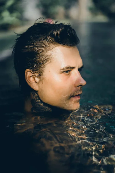 young handsome man in tattoos resting in the outdoor pool. A tattooed man in the pool is having fun. on bali, indonesia