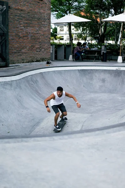 Bir havuzda pateni bir şık genç adam bir skatepark, bir kaykay üzerinde beyaz bir T-shirt ve şapka paten.