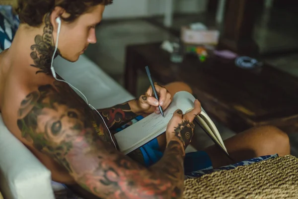 Молодий Чоловік Татуюваннях Навушниках Слухає Музику Малює Олівець Блокноті Онлайн — стокове фото