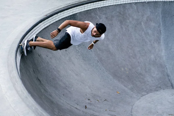 Bir havuzda pateni bir şık genç adam bir skatepark, bir kaykay üzerinde beyaz bir T-shirt ve şapka paten.