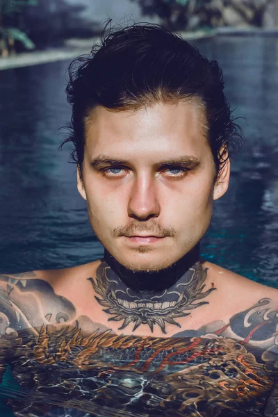 young handsome man in tattoos resting in the outdoor pool. A tattooed man in the pool is having fun. on bali, indonesia