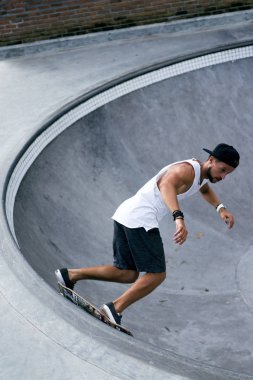 Bir havuzda pateni bir şık genç adam bir skatepark, bir kaykay üzerinde beyaz bir T-shirt ve şapka paten.