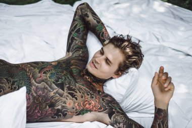 yakışıklı, Genç bir dövmeli adam sabah yatakta yastık fırlatır. Bahçe yatağında