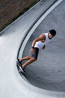 Bir havuzda pateni bir şık genç adam bir skatepark, bir kaykay üzerinde beyaz bir T-shirt ve şapka paten.