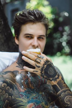 Genç yakışıklı adam açık havada bahçede açık havada yatakta kahvaltı dövme