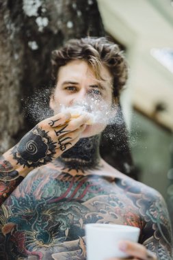 Genç yakışıklı adam açık havada bahçede açık havada yatakta kahvaltı dövme