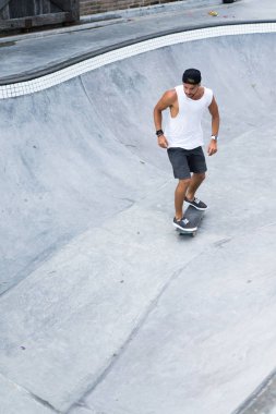Bir havuzda pateni bir şık genç adam bir skatepark, bir kaykay üzerinde beyaz bir T-shirt ve şapka paten.