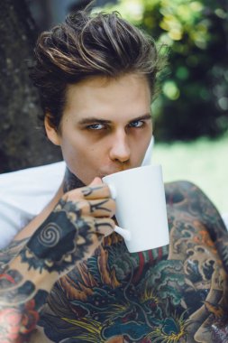 Genç yakışıklı adam açık havada bahçede açık havada yatakta kahvaltı dövme