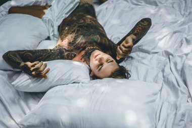 Yakışıklı genç dövmeli adam beyaz yatakta rahatlatıcı