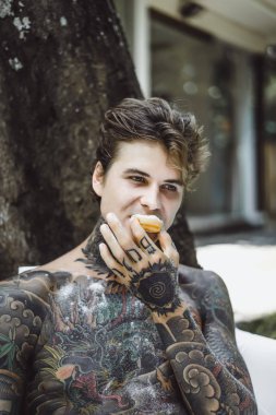 Genç yakışıklı adam açık havada bahçede açık havada yatakta kahvaltı dövme