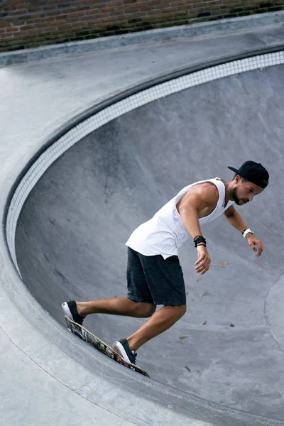 Bir havuzda pateni bir şık genç adam bir skatepark, bir kaykay üzerinde beyaz bir T-shirt ve şapka paten.