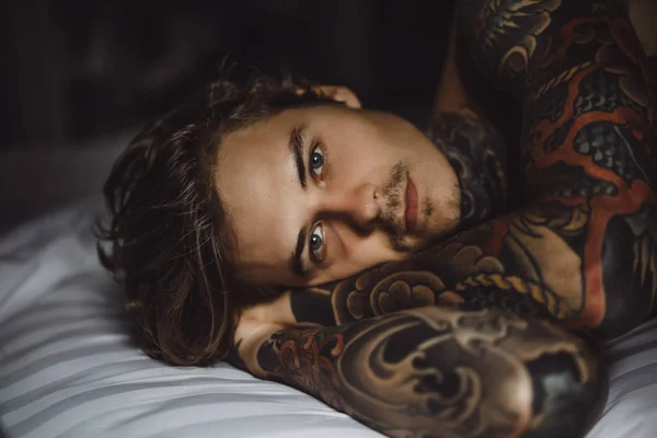 Handsome young tattooed man relaxing on white bed