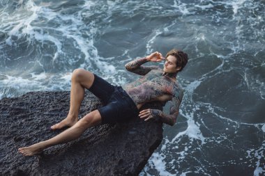 Bir uçurumun kenarında dövmeli bir adam. okyanus dalgaları sıçraması. 