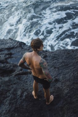 Bir uçurumun kenarında dövmeli bir adam. okyanus dalgaları sıçraması. 