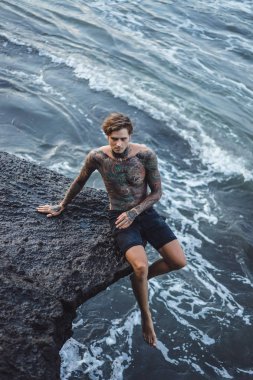 Bir uçurumun kenarında dövmeli bir adam. okyanus dalgaları sıçraması. 