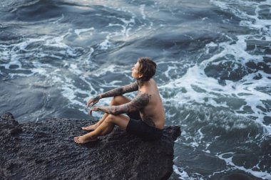 Bir uçurumun kenarında dövmeli bir adam. okyanus dalgaları sıçraması. 