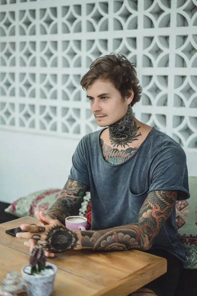 tattooed man drinking coffee in a cafe