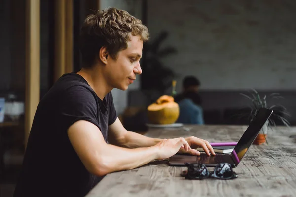 man working at a laptop in a cafe on a wooden table, hands of a man working on a computer, smartphone, notebook, desktop.