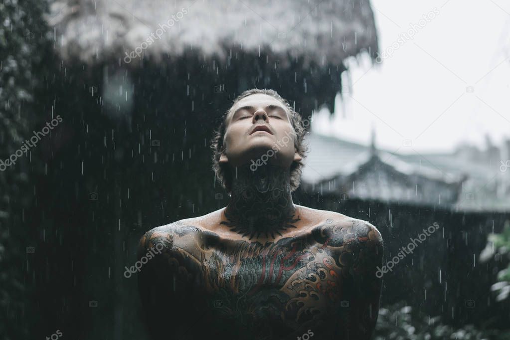 young tattooed man posing in the rain