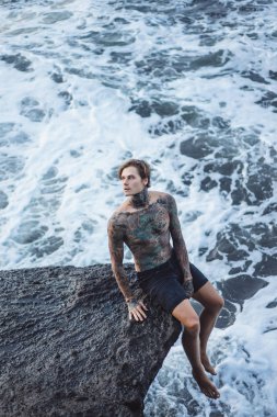 Bir uçurumun kenarında dövmeli bir adam. okyanus dalgaları sıçraması. 