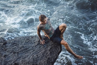 Bir uçurumun kenarında dövmeli bir adam. okyanus dalgaları sıçraması. 