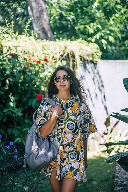 bir sırt çantası, güneş gözlüğü, tropikal bahçede giyen kızla