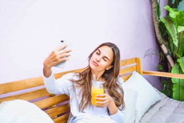 Güzel bir kadın bir kafede selfie Smartphone'da yapar, taze sıkılmış meyve suyu içecekler.