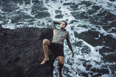 Bir uçurumun kenarında dövmeli bir adam. okyanus dalgaları sıçraması. 