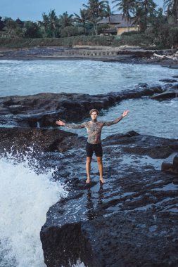 Bir uçurumun kenarında dövmeli bir adam. okyanus dalgaları sıçraması. 