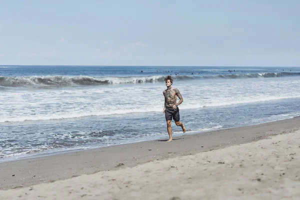 海の海岸に男性の刺青は 海岸に沿って実行しているスポーツに取り組んでいます 海岸のスポーツの概念 — ストック写真