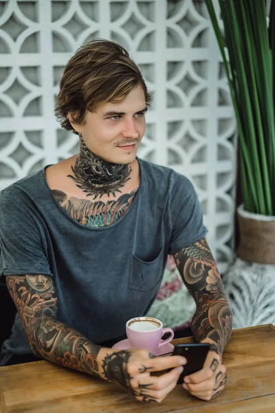 tattooed man drinking coffee in a cafe