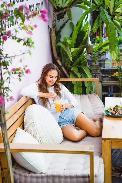 A beautiful woman has breakfast in a stylish cafe, a healthy breakfast, fruit, freshly squeezed juice, tropical location.