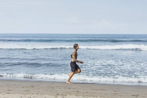 海の海岸に男性の刺青は 海岸に沿って実行しているスポーツに取り組んでいます 海岸のスポーツの概念 — ストック写真