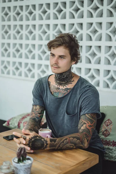 tattooed man drinking coffee in a cafe
