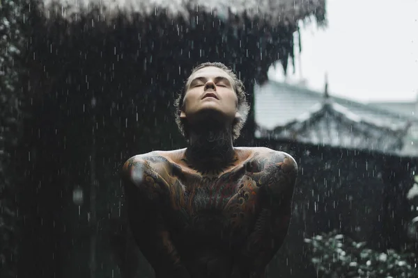 young tattooed man posing in the rain