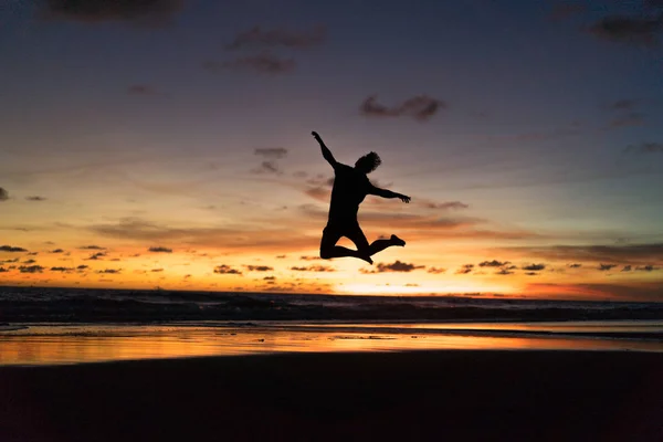 person on the shore of the ocean at sunset. man jumps against the backdrop of the setting sun.