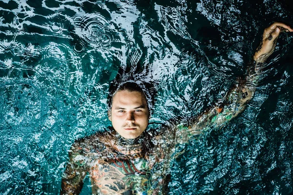 tattooed man in the pool in the rain. close-up, portrait, outdoors
