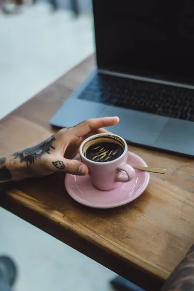 tattooed hands of man. drinking coffee and using laptop concept